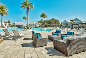 Zona de piscina con sillones de descanso y mobiliario de mimbre, rodeada de palmeras y un cielo azul despejado.