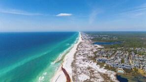 Eine Luftaufnahme einer Küstenregion mit Strand, Wohnhäusern und einem großen Gewässer.