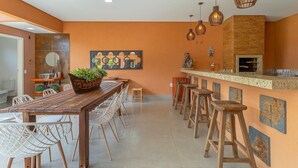 Una cocina moderna con una mesa de madera y taburetes de bar, un horno para pizza e iluminación colgante.