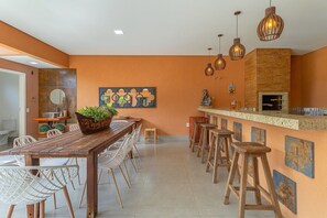 Een moderne keuken met een houten tafel en barstoelen, een pizzaoven en hanglampen.