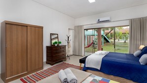 Un dormitorio con un armario grande, una cama con colcha azul, un tapete a rayas y vistas a un patio de recreo.
