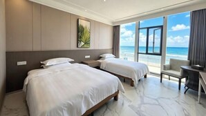 A hotel room with two beds, a balcony with a view of the beach, and a desk with a chair. - Bao'an Rainbow Bay Hotel (Huidong)