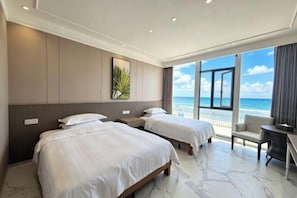 Une chambre d’hôtel avec deux lits, un balcon donnant sur la plage et un bureau avec une chaise.