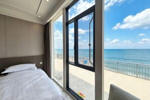 A hotel room with a large window, a bed, and a view of the beach.