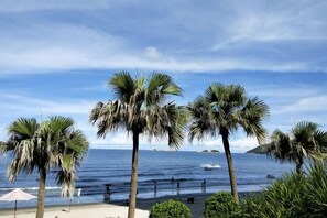 A beach with palm trees, a boat in the water, and a clear sky.