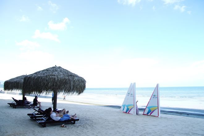 Una playa con una sombrilla de paja, sillas de descanso y tablas de vela.
