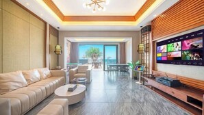 A modern living room with a sofa, coffee table, flat-screen TV, and a balcony with a view. - Bao'an Rainbow Bay Hotel (Huidong)