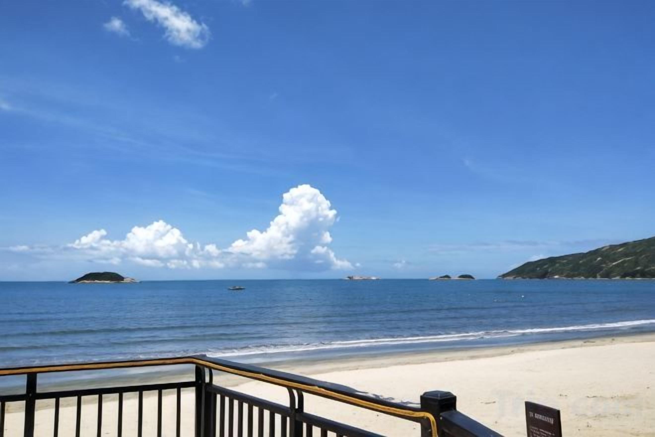 Ein Strand mit blauem Himmel, sandigem Ufer und einer Geländer.
