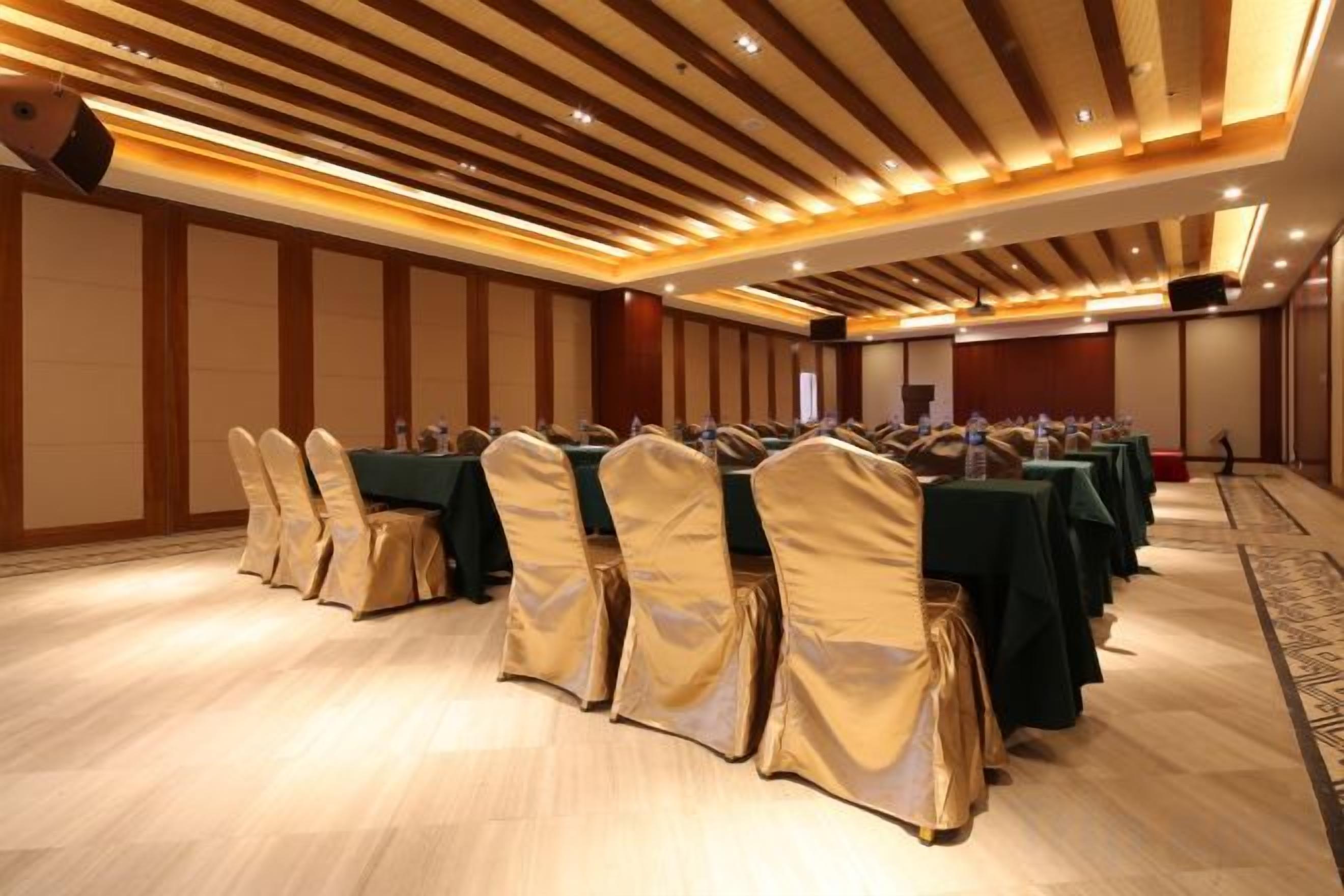 A conference room with rows of tables and chairs, a wooden ceiling, and a carpeted floor.