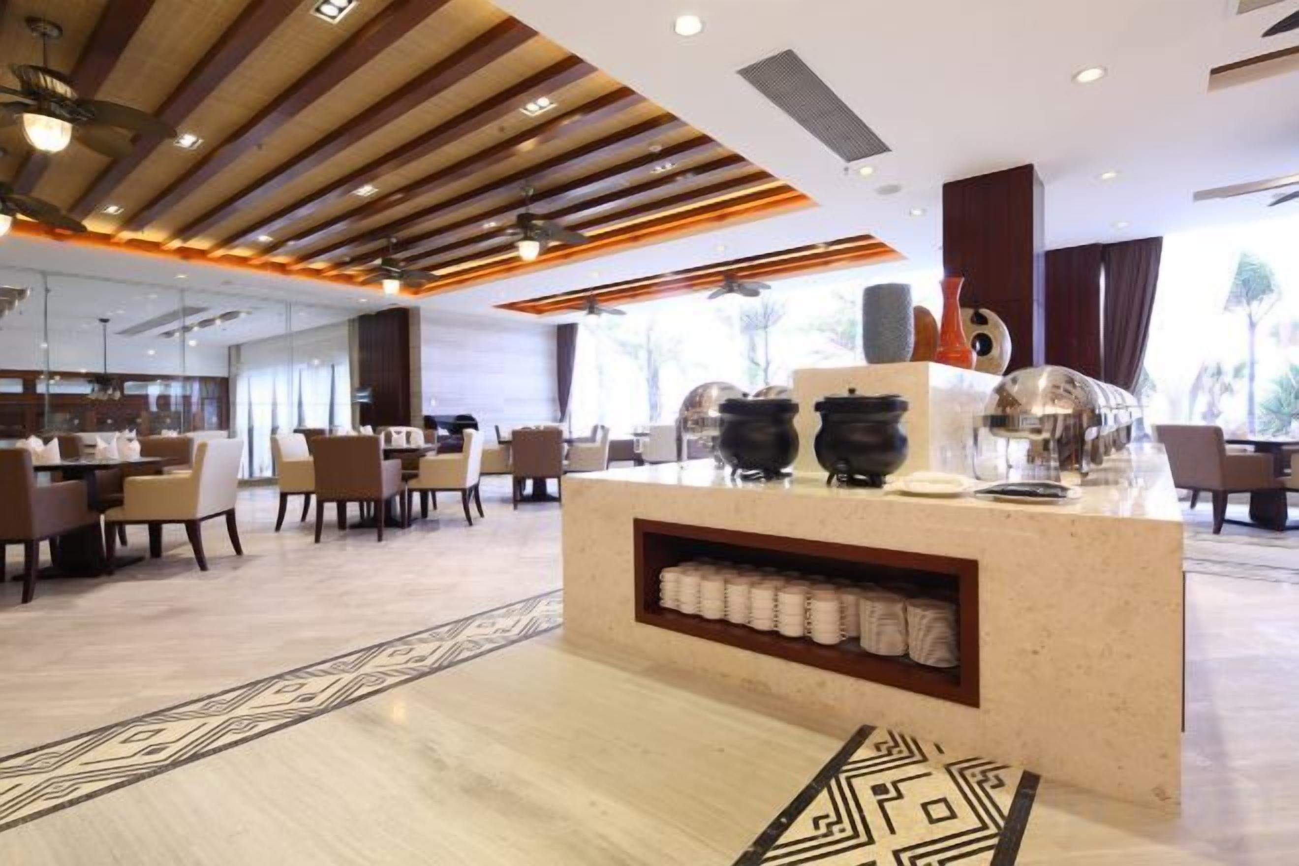 A modern hotel lobby with a central reception desk, seating area, and large windows.