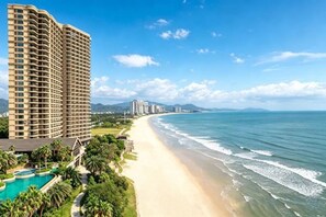 Un hotel frente a la playa con piscina, vista al océano y un edificio alto al fondo.