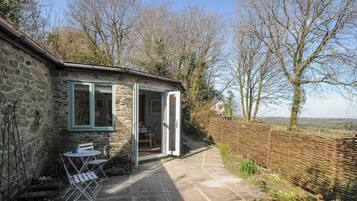 A stone cottage with a small patio, a table and chairs, and a view of the countryside.