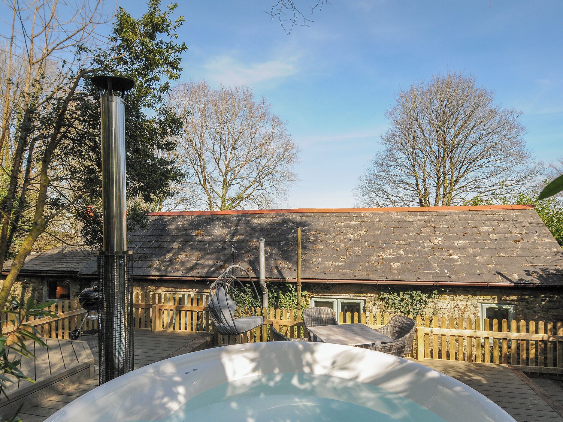 A hot tub in a backyard with a wooden fence, a brick building, and trees.