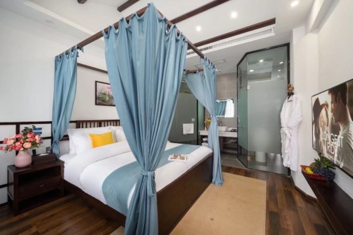 A bedroom with a four-poster bed, a bedside table with a vase of flowers, and a large mirror.