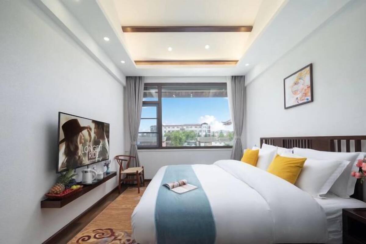 Ein Hotelzimmer mit Bett, Fernseher, Fenster mit Blick und einem kleinen Tisch mit Obstplatte.