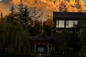 A traditional building with a modern extension, surrounded by trees and a mountain backdrop. - Banmu Fangtang Inn in Lijiang (Lijiang)