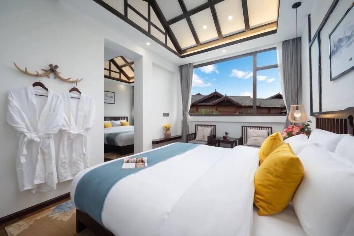 Ein Hotelzimmer mit Bett, einem Fenster mit Blick auf traditionelle Architektur und einem Kleiderständer mit Bademänteln.