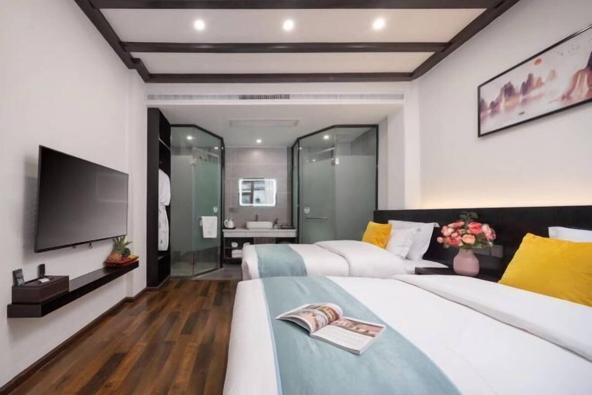Ein modernes Hotelzimmer mit Flachbildfernseher, einem Bett mit blauer Decke, einem Nachttisch und einem an der Wand montierten Fernseher.