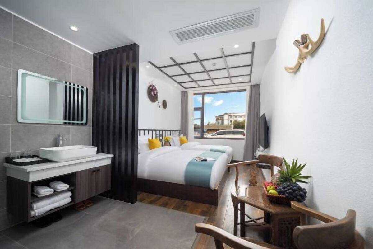 Ein modernes Hotelzimmer mit einem großen Bett, einem Badezimmer mit Waschbecken und Spiegel, einem Esstisch mit Stühlen und Blick auf die Stadt.
