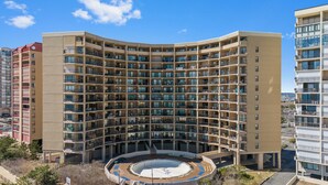 A multi-story hotel with a curved facade, numerous balconies, and a central courtyard. - Bright Oceanfront Studio | Sleeps 4 w/ Pool Access (Ocean City)