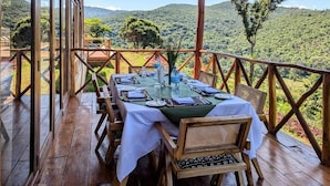 A wooden deck with a table set for dining, overlooking a hilly landscape. - Mvuli Mountain Lodge Ngorongoro (Karatu)