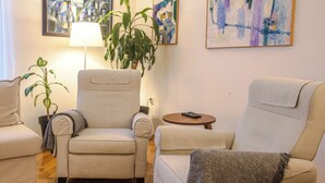 A living room with two armchairs, a floor lamp, a potted plant, and artwork on the wall.