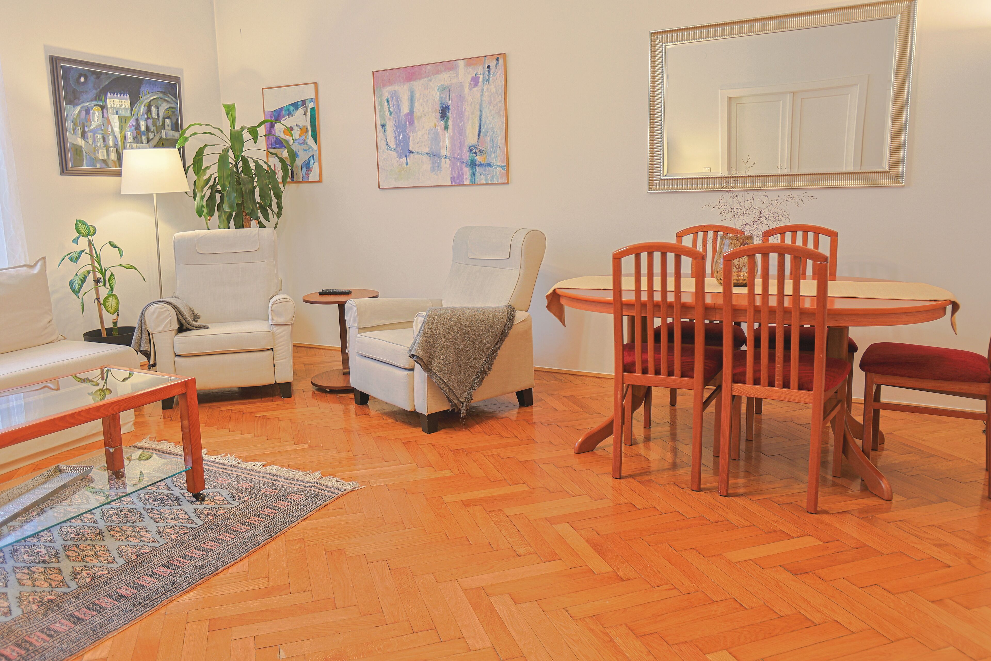 Een woonkamer met een bank, fauteuil, eettafel met stoelen, een lamp en een plant.