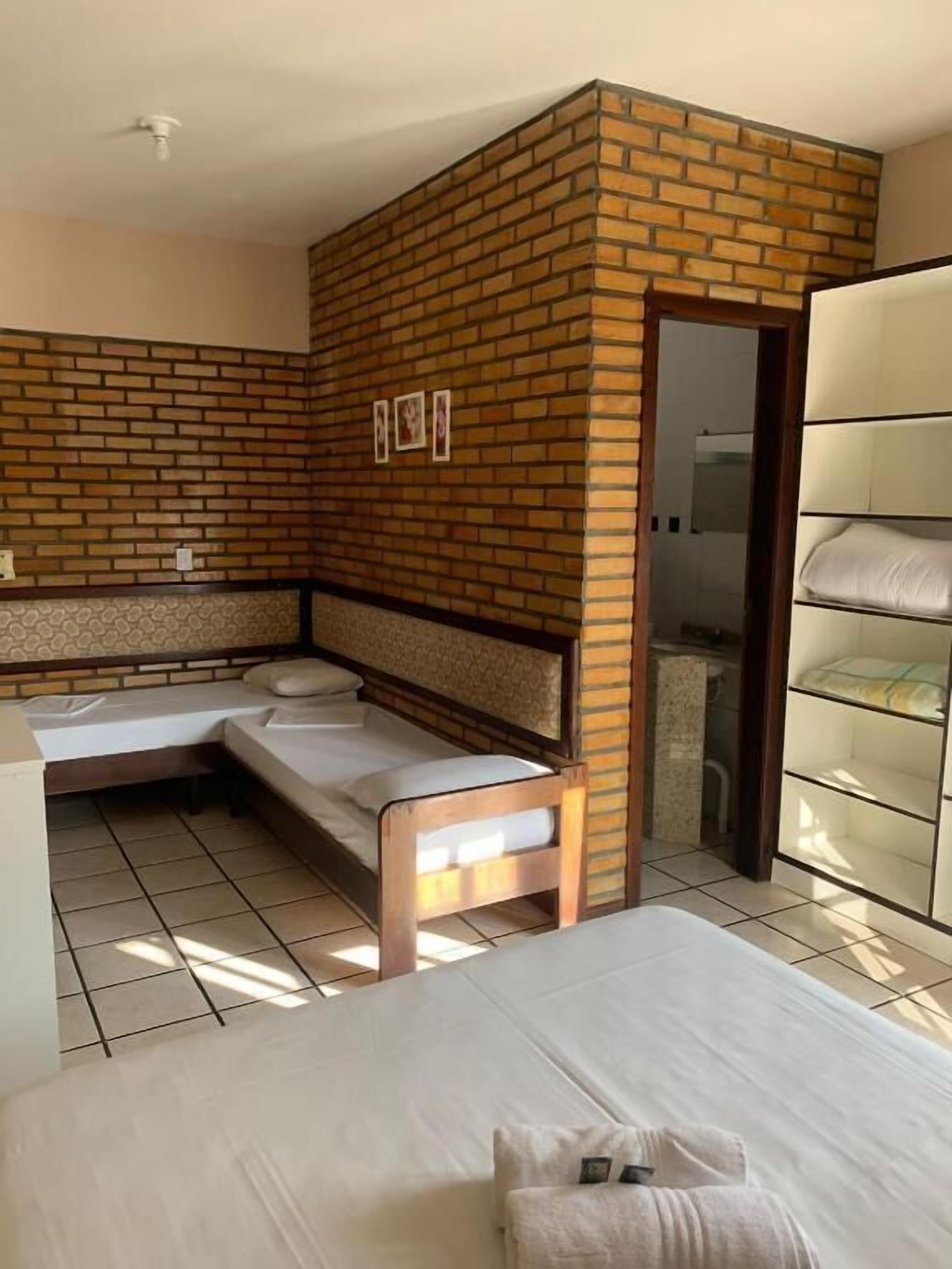 A room with a brick accent wall, a bed, a bench, and a wardrobe.