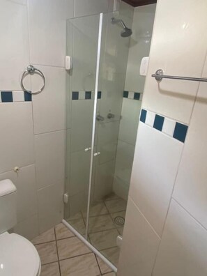 A small bathroom with a glass shower enclosure, a toilet, and a towel rack.