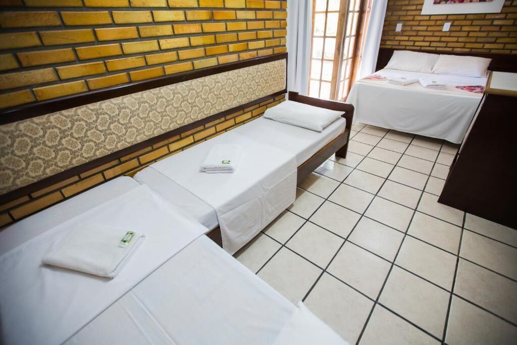 A hotel room with two single beds, a brick wall, a patterned wallpaper section, and a tiled floor.
