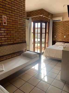 A room with a brick wall, a bed, a small sofa, and a window with curtains. - Hotel D luz (Itapema)
