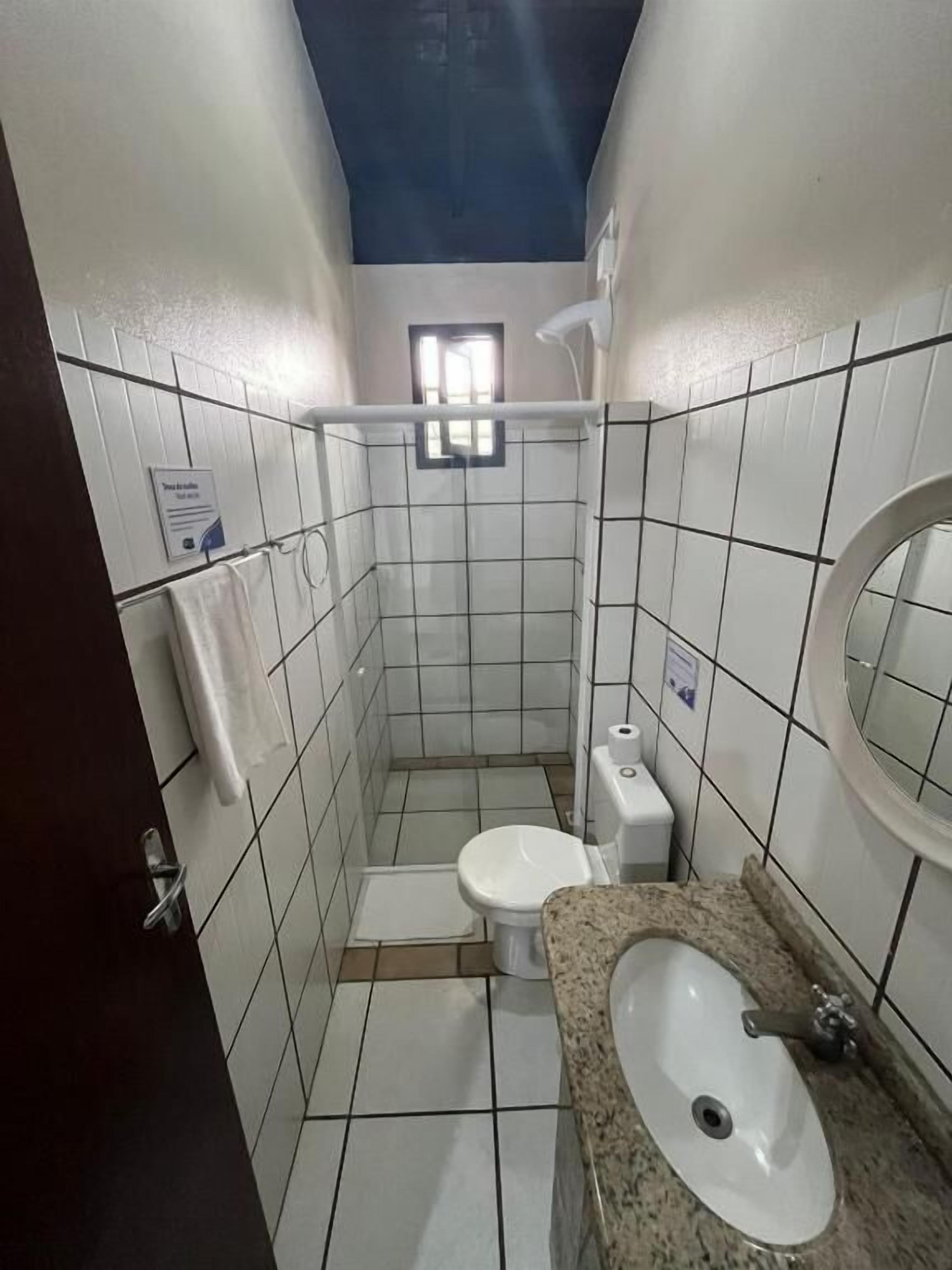 Une petite salle de bain carrelée, équipée de toilettes, d’un lavabo et d’une fenêtre.