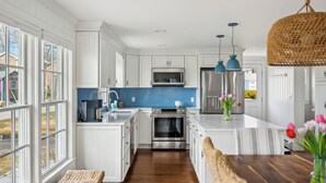 A modern kitchen with white cabinets, a blue backsplash, stainless steel appliances, and large windows. - Ocean Views! Walk to Beaches! 4BR Vacation Retreat (Kennebunk)