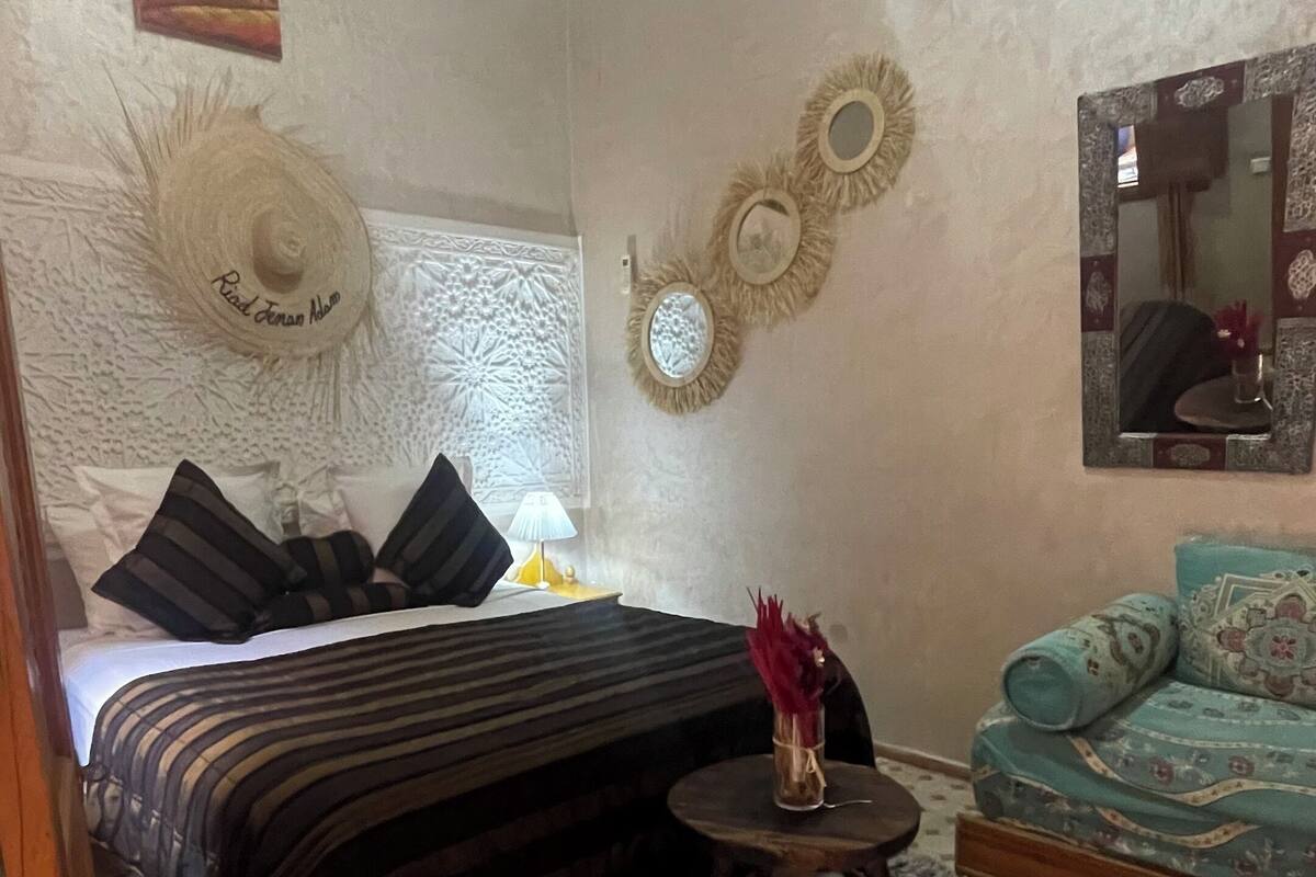 A bedroom with a bed, a small round table with a vase, a sofa, and decorative wall art.