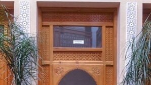 Una entrada tradicional marroquí con elaboradas tallas de madera, suelo de mosaicos y plantas en macetas.