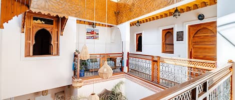 A multi-level interior with ornate wooden railings, a hanging light fixture, and a view of the outside.