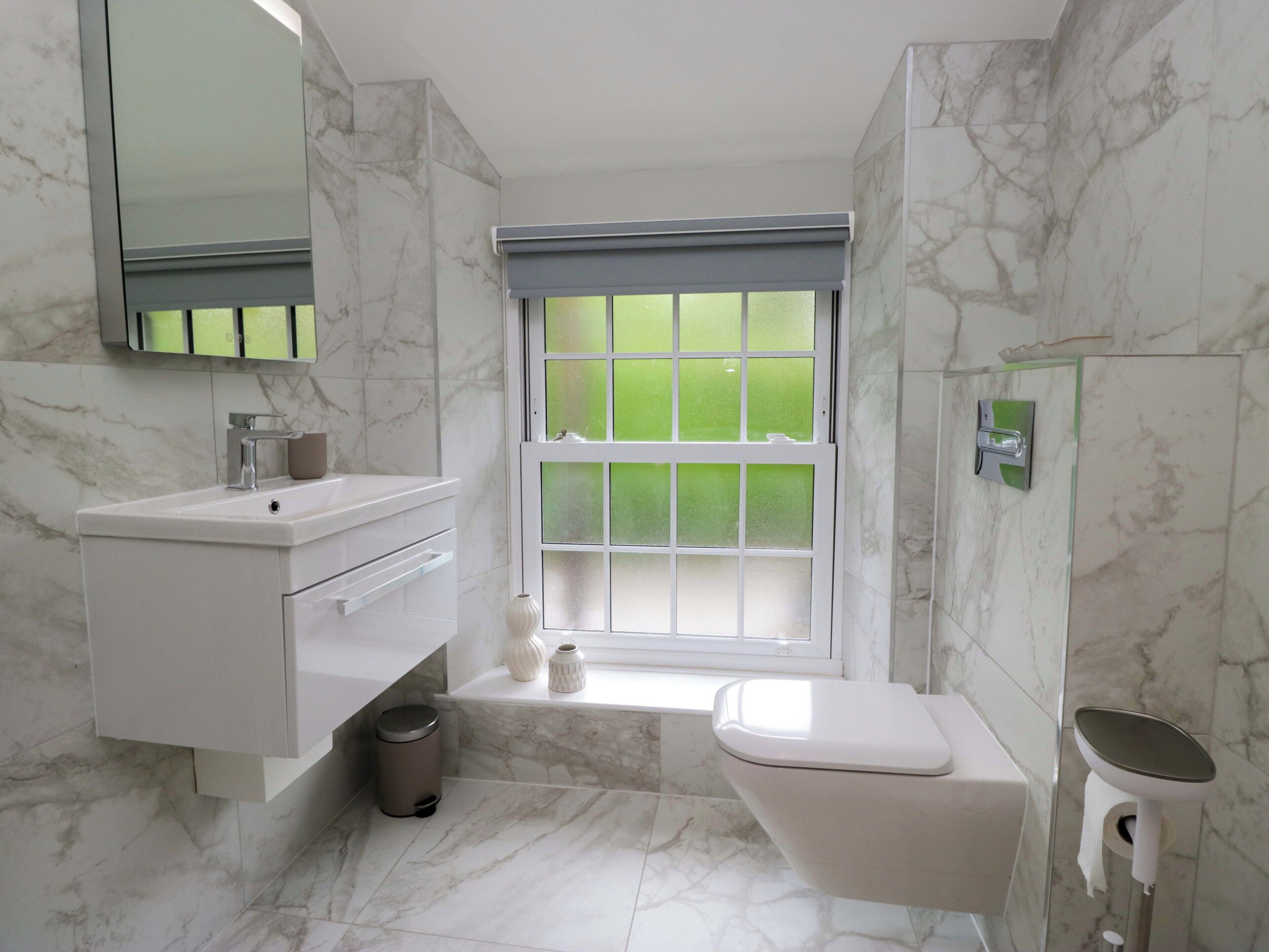A bathroom with a marble floor, a white sink, a toilet, and a window with frosted glass.