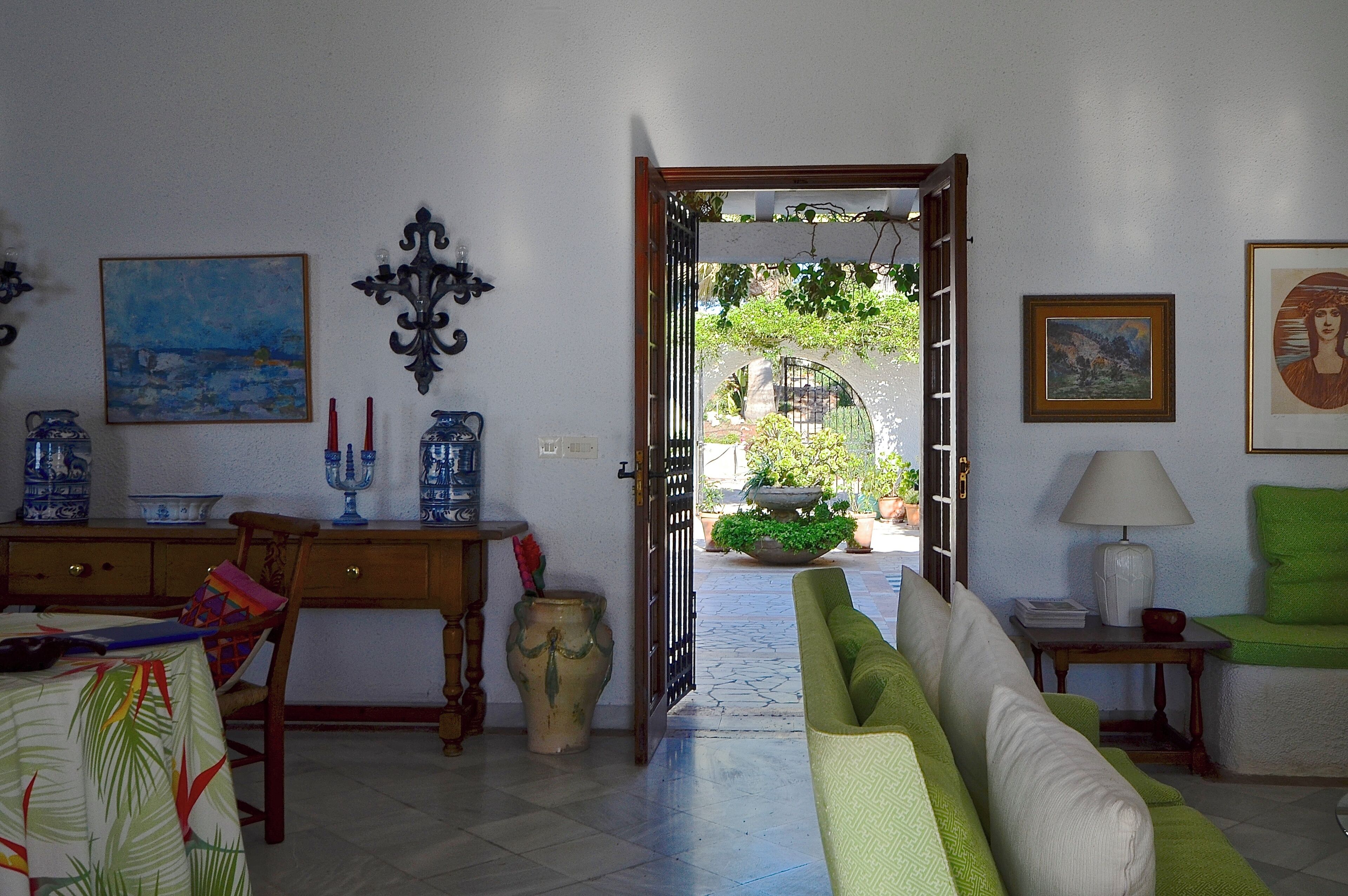 A room with a dining area, a green sofa, and a view through an open door to a garden.