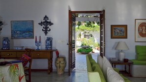A room with a dining area, a green sofa, and a view through an open door to a garden.