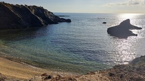 A coastal landscape with clear water, rocky cliffs, and a sandy beach.