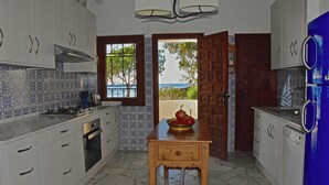 A kitchen with white cabinets, a wooden table, and a view of the sea through a window.