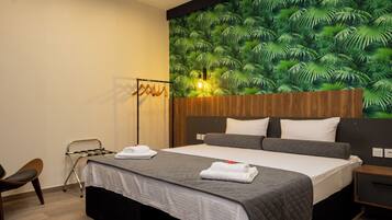 Habitació d'hotel amb llit, una petita taula de nit, una cadira i una paret amb un disseny de fulles tropicals.