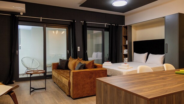 A modern hotel room with a wooden floor, a sofa, a bed, a desk, and a chair. - Dioroh Suites Meteora 304 (Kalabaka)