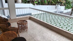 Un balcon doté de meubles en osier, d’un sol carrelé et d’une balustrade blanche.