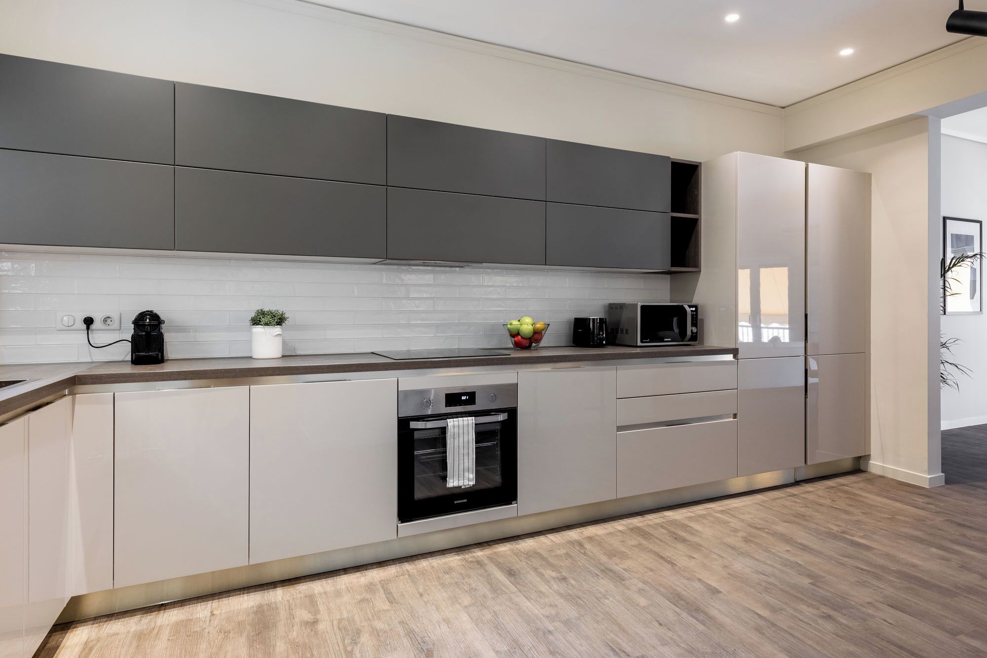 A modern kitchen with grey cabinets, a built-in oven, a microwave, and a coffee maker.