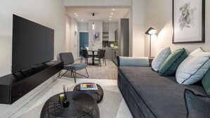 Ein modernes Wohnzimmer mit Flachbildfernseher, einer Couch, einem Couchtisch und einem Essbereich im Hintergrund.