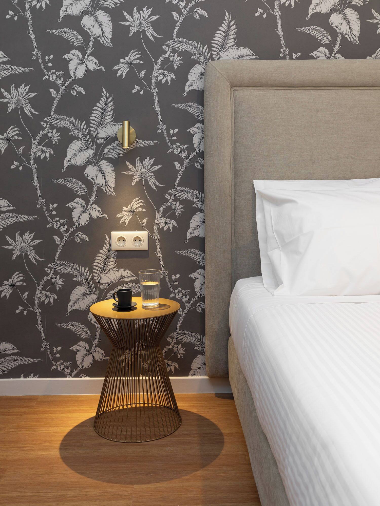 Ein Schlafzimmer mit einem Bett, einem Nachttisch mit Lampe und einer Wand mit Blumenmuster.