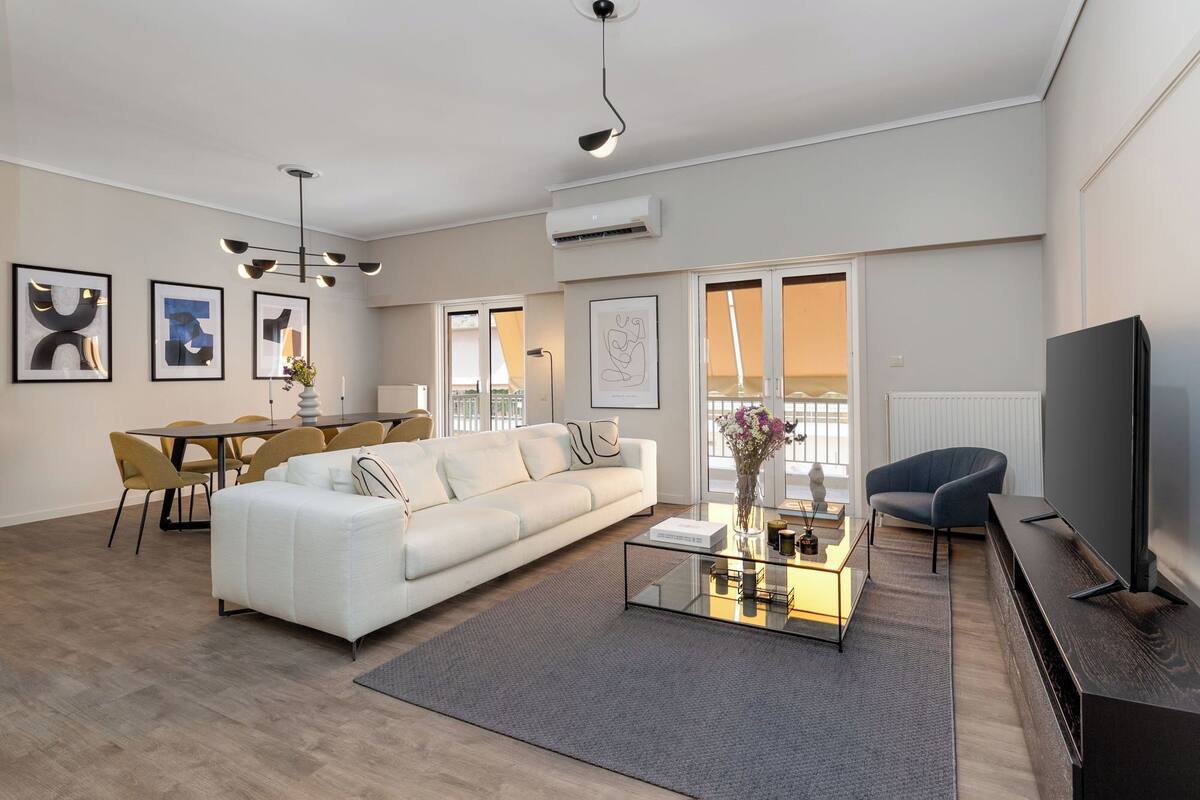 A modern living room with a white sofa, a glass coffee table, and a flat-screen TV.