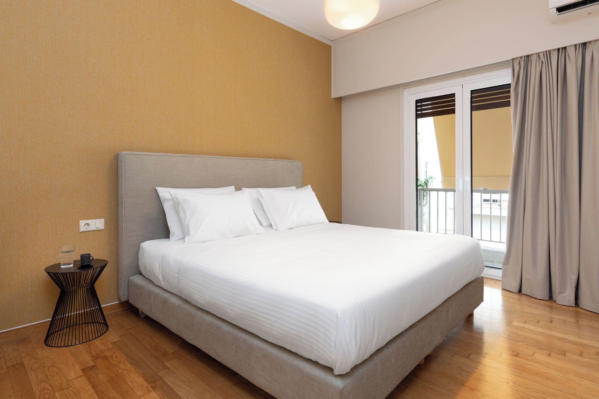 A modern hotel room with a large bed, a small side table, and a balcony with curtains.