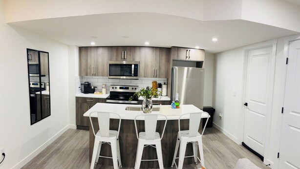 Una cocina moderna con una isla central, taburetes blancos para bar y una mesa de comedor.